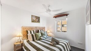 Ein Schlafzimmer mit Bett, Deckenventilator, Fenster und Nachttisch mit Lampe.