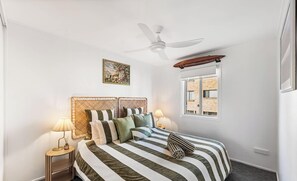 A bedroom with a bed, a ceiling fan, a window, and a nightstand with a lamp. - Absolute Broadwater Escape (Labrador)