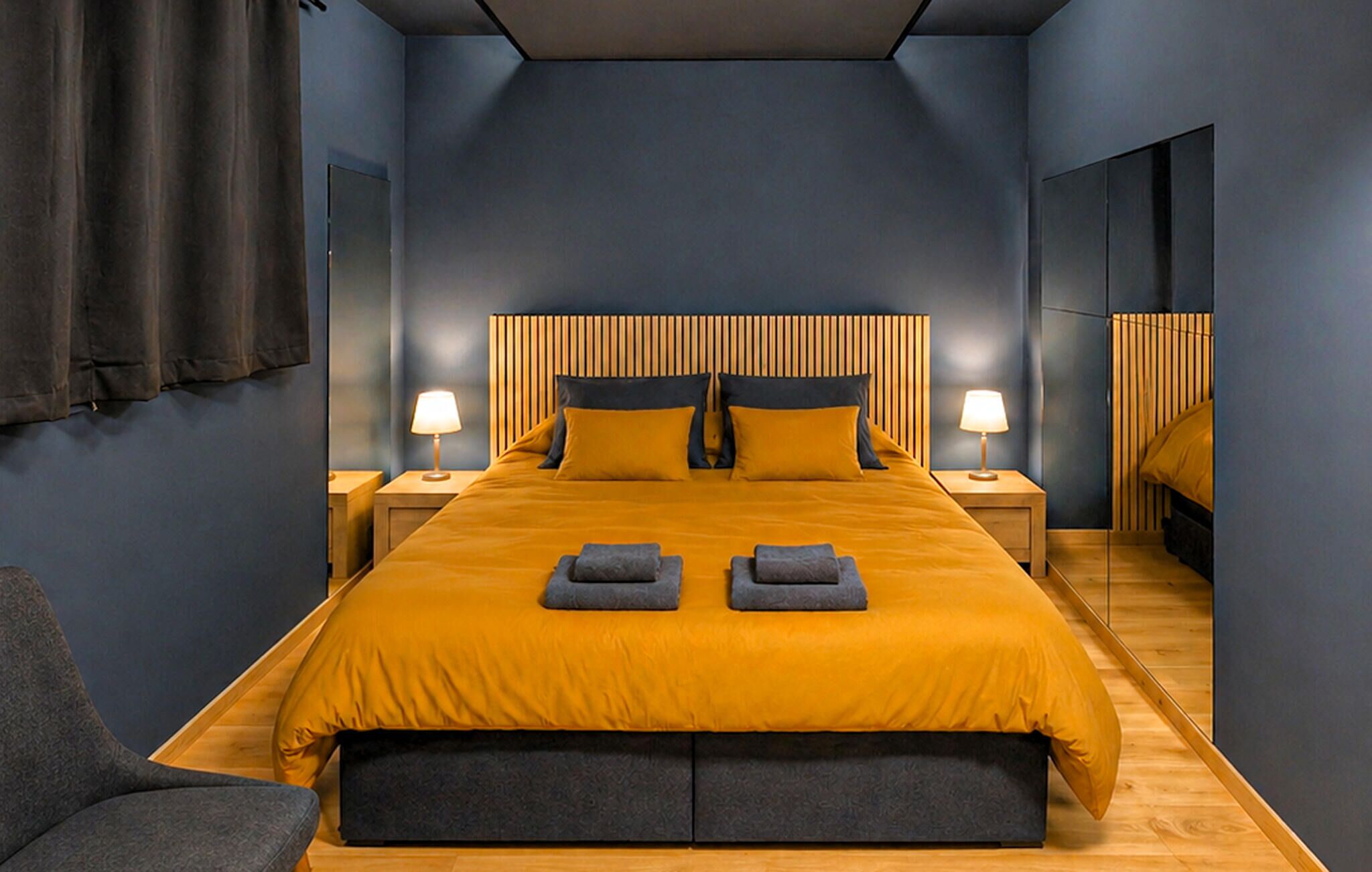 A modern hotel room with a large bed, two bedside tables, a mirror, and a chair.