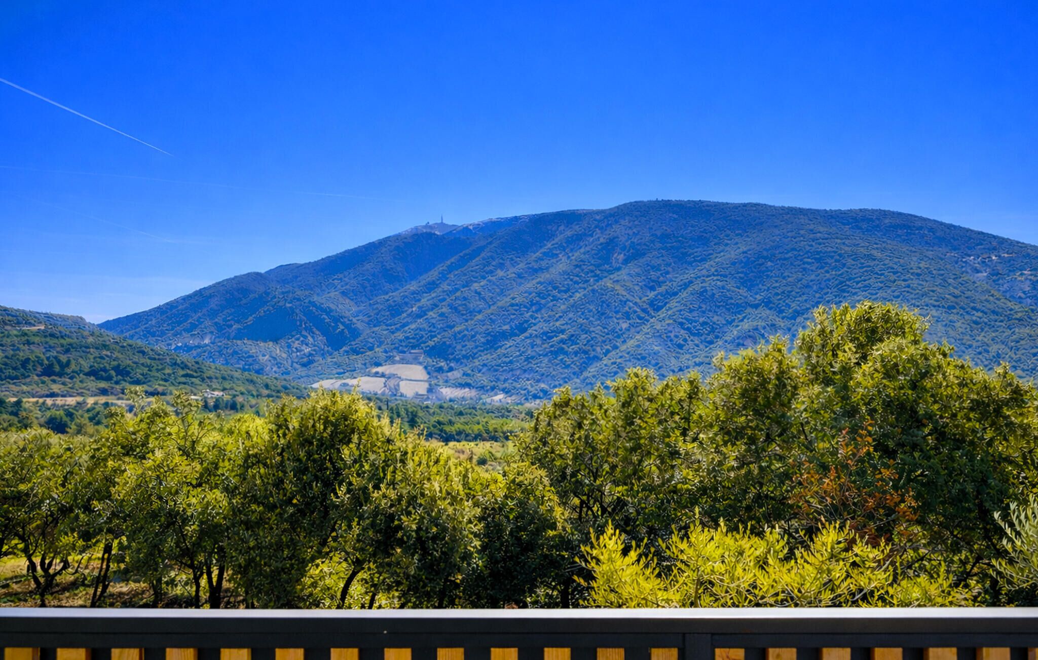 Paisagem montanhosa com vegetação densa em primeiro plano e céu azul límpido.