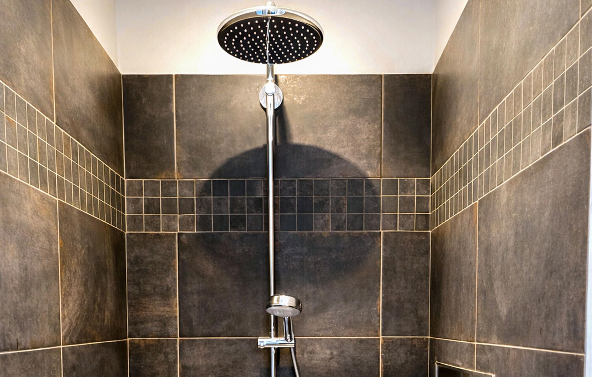 A shower with a rain shower head, tiled walls, and a tiled floor.