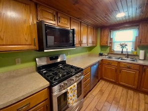 A kitchen with wooden cabinets, a microwave, stove, oven, and a window with blinds.