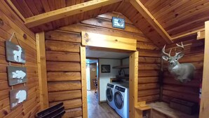 Ein Interieur einer Blockhütte mit einer Holzbank, einem an der Wand befestigten Hirschkopf und einem Schild, das einen Jagdrevier kennzeichnet.