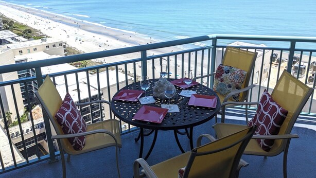 Ein Balkon mit Tisch und Stühlen mit Blick auf einen Strand.