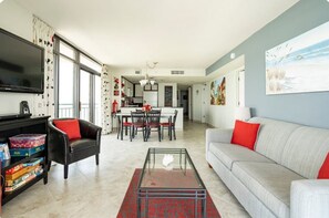 A modern living room with a sofa, a coffee table, a TV, and a bookshelf. - Best Views! Penthouse 3BD/3BA Corner Unit w/ Huge Wrap-Around Balcony (Myrtle Beach)