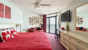 Ein Hotelzimmer mit einem großen Bett, einem Schreibtisch, einem Sessel, einem Fernseher, einem Deckenventilator und einem Balkon mit Blick.