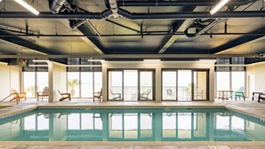 Ein Hallenbad mit großen Glaswänden, Stühlen und einer Decke mit freiliegenden Rohren.