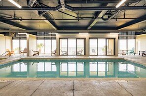An indoor swimming pool with clear glass walls, chairs, and a ceiling with exposed pipes. - Best Views! Penthouse 3BD/3BA Corner Unit w/ Huge Wrap-Around Balcony (Myrtle Beach)
