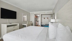 Habitació d'hotel amb llit, televisió, escriptori, cadira, taula petita i bany visible per una porta oberta.