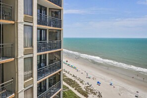A multi-story building with balconies overlooking a beach with umbrellas and people. - Oceanfront King Studio + Beach Access + Lazy River (Myrtle Beach)