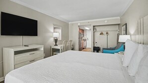 A hotel room with a large bed, a TV mounted on the wall, a desk with a lamp, and a chair. - Oceanfront King Studio + Beach Access + Lazy River (Myrtle Beach)
