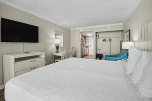A hotel room with a large bed, a TV mounted on the wall, a desk with a lamp, and a chair. - Oceanfront King Studio + Beach Access + Lazy River (Myrtle Beach)