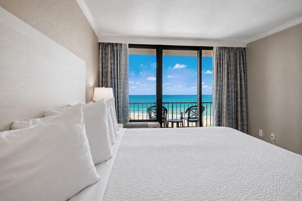 Ein Hotelzimmer mit einem großen Bett, Meerblick und einem Balkon mit Sitzgelegenheiten.