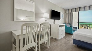 Habitación de hotel con cama, escritorio, sillas, televisor y balcón con vistas.