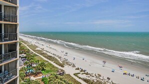 Vista de la playa desde un edificio alto con balcones, una playa de arena y olas oceánicas.