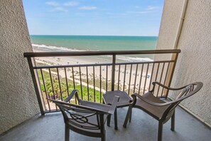 Un balcon avec vue sur la plage, une table et deux chaises.