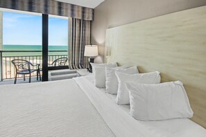 Une chambre d’hôtel avec un grand lit, une vue sur la plage et un balcon équipé de chaises.