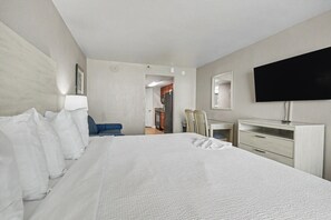 A hotel room with a large bed, a desk, a chair, a television, and a wardrobe. - Oceanfront King Studio w/ Sleeper Sofa + Pools (Myrtle Beach)