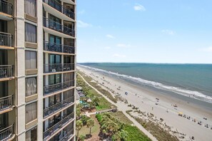 A high-rise building with multiple balconies overlooking a beach. - Oceanfront King Studio w/ Sleeper Sofa + Pools (Myrtle Beach)