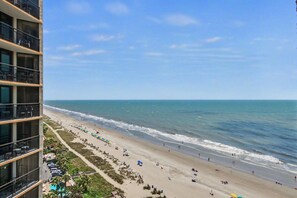 A beach with a high-rise building in the foreground. - Oceanfront King Studio w/ Sleeper Sofa + Pools (Myrtle Beach)