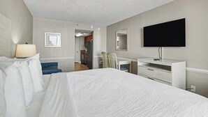 Habitación de hotel con cama, escritorio, silla, televisor y espejo.