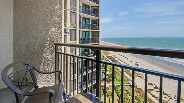 Un balcón con vista a la playa, una silla y un edificio con varios balcones.
