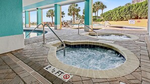 Zona de hidromasaje con un cartel de prohibición de buceo, un anuncio de servicio de socorrista y una piscina con sillones de descanso.