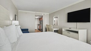 A hotel room with a large bed, a desk, a chair, a flat-screen TV, and a view into the kitchen area. - Oceanfront King Studio w/ Sleeper Sofa + Pools (Myrtle Beach)