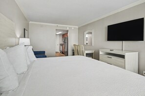 A hotel room with a large bed, a desk, a chair, a flat-screen TV, and a view into the kitchen area. - Oceanfront King Studio w/ Sleeper Sofa + Pools (Myrtle Beach)