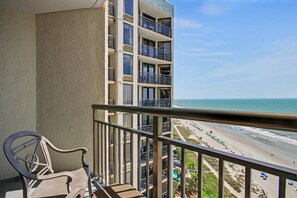 A balcony with a view of a beach and a multi-story building. - Oceanfront King Studio w/ Sleeper Sofa + Pools (Myrtle Beach)