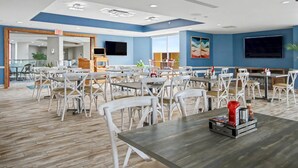 A spacious dining area with multiple tables and chairs, a flat-screen TV mounted on the wall, and a wooden floor. - Oceanfront King Studio w/ Sleeper Sofa + Pools (Myrtle Beach)