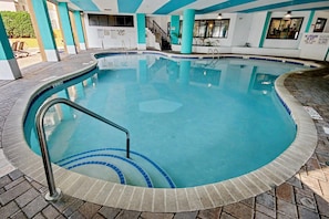 Une piscine intérieure avec un bord carrelé, une échelle en métal et un escalier menant à un niveau supérieur.