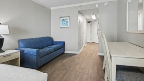 Ein Hotelzimmer mit einem blauen Sofa, einem Holztisch, einem weißen Schreibtisch und einem Spiegel.
