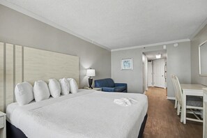 Hotellihuone, jossa on suuri sänky, työpöytä, tuoli, lamppu ja seinällä oleva kehystetty kuva.