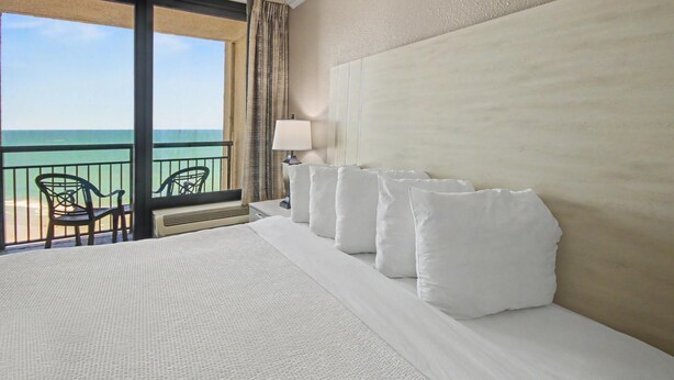 Ein Hotelzimmer mit einem großen Bett, Meerblick und einem Balkon mit Stühlen.