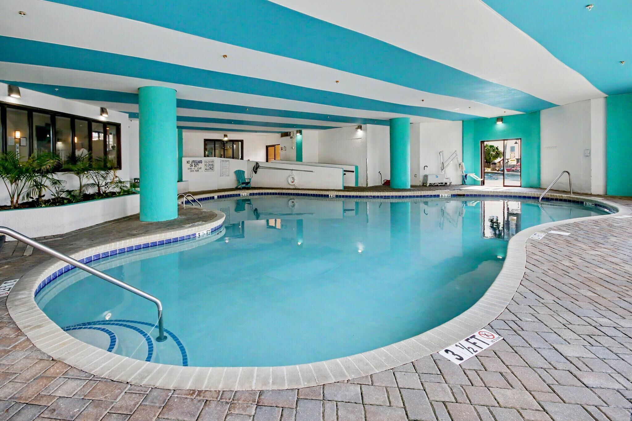 An indoor swimming pool with a tiled edge, a lifeguard chair, and a pool ladder.