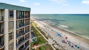 Un hotel de altura con balcones que dan a una playa con sombrillas y gente.
