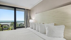 Un cuarto de hotel con una cama grande, un balcón con sillas y vista al océano.