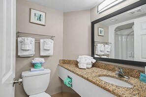 A bathroom with a toilet, sink, and mirror. There are towels hanging on a rack and a picture on the wall. - Oceanfront King Studio w/ Sleeper Sofa + Pools (Myrtle Beach)