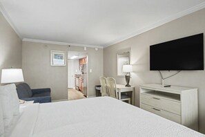 A hotel room with a bed, a desk, a chair, a TV, and a bathroom visible through an open door. - Oceanfront King Studio w/ Sleeper Sofa + Pools (Myrtle Beach)
