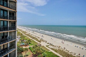 A beach with a view of the ocean, a building with balconies, and a clear sky. - Oceanfront King Studio w/ Sleeper Sofa + Pools (Myrtle Beach)