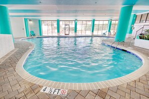 Ein Hallenbad mit einer maximalen Wassertiefe von 1,40 Metern, umgeben von Fliesenboden und -wänden, mit Blick ins Freie durch große Fenster.