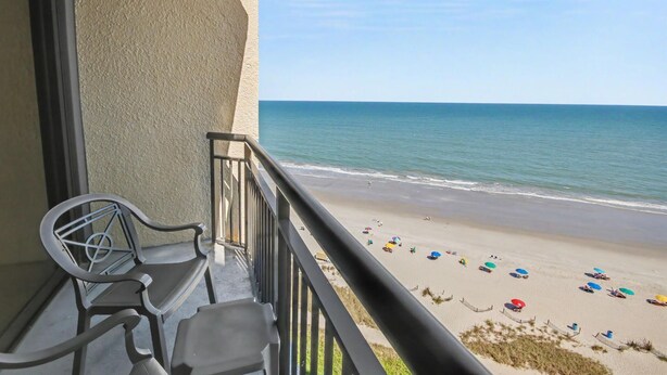 A balcony with a view of a beach, a chair, and a table. - Oceanfront Studio w/ Two Queens + Beach & Pools (Myrtle Beach)