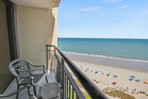 A balcony with a view of a beach, a chair, and a table. - Oceanfront Studio w/ Two Queens + Beach & Pools (Myrtle Beach)