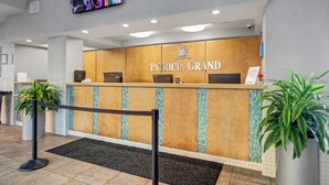 A reception desk with a 'Patricia Grand' sign, a mounted television, and potted plants. - Oceanfront Studio w/ Two Queens + Beach & Pools (Myrtle Beach)