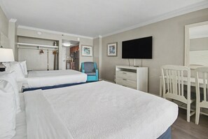 Ein Hotelzimmer mit zwei Betten, einem Schreibtisch, einem Sessel, einem Fernseher und einem durchgegangenen Badezimmer.