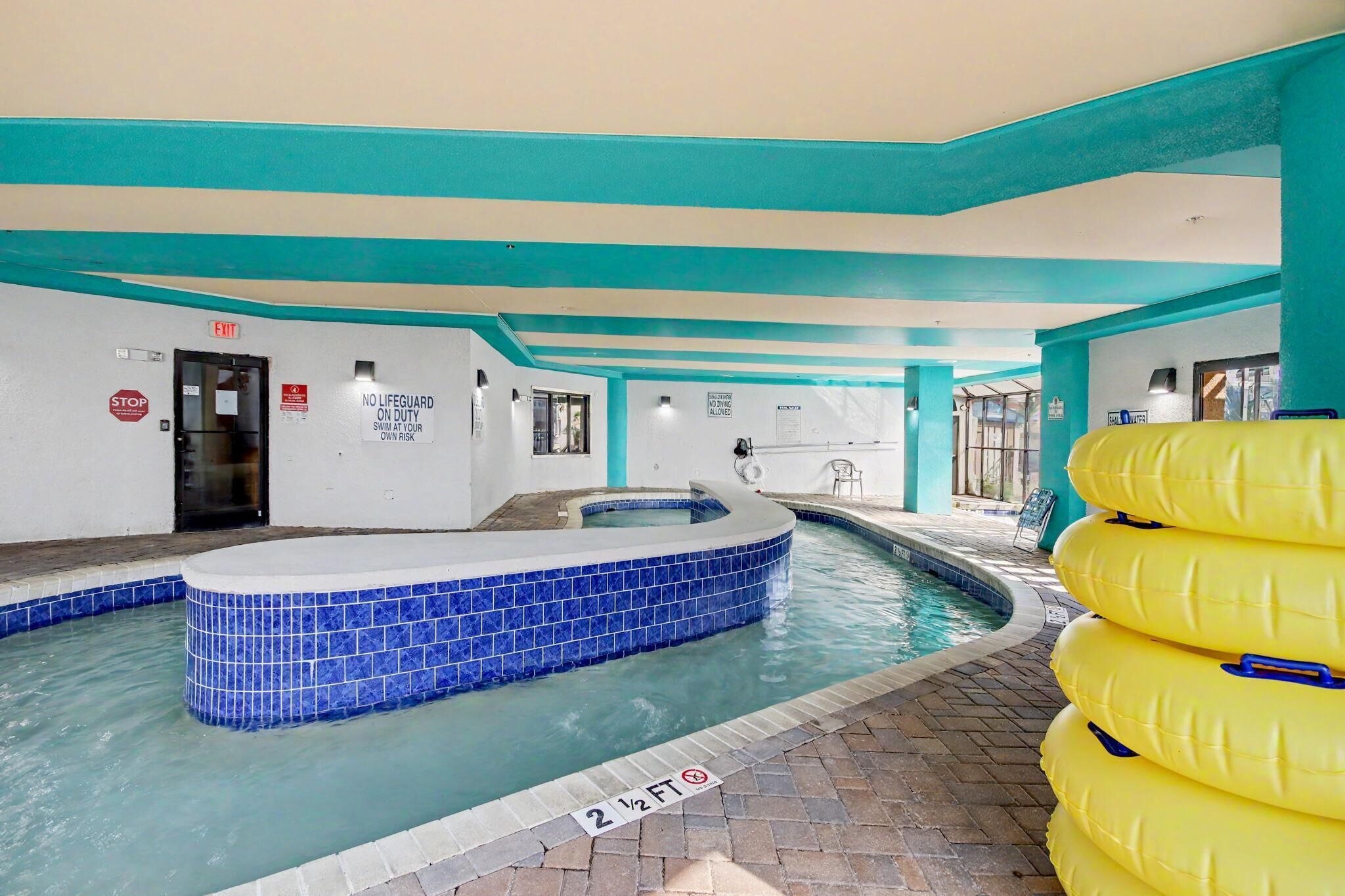 Une piscine intérieure avec un espace de jacuzzi aux carreaux bleus, un poste de surveillance pour les sauveteurs et un panneau indiquant l’absence de sauveteur.