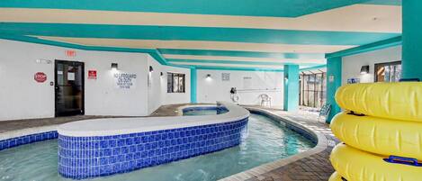 Une piscine intérieure avec un espace de jacuzzi aux carreaux bleus, un poste de surveillance pour les sauveteurs et un panneau indiquant l’absence de sauveteur.