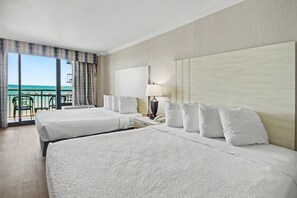 A hotel room with two beds, a nightstand, a lamp, and a view of the ocean through large windows. - Oceanfront Studio w/ Two Queens + Beach & Pools (Myrtle Beach)