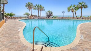 Una piscina con acqua cristallina, circondata da lettini prendisole e palme, con vista sull'oceano.